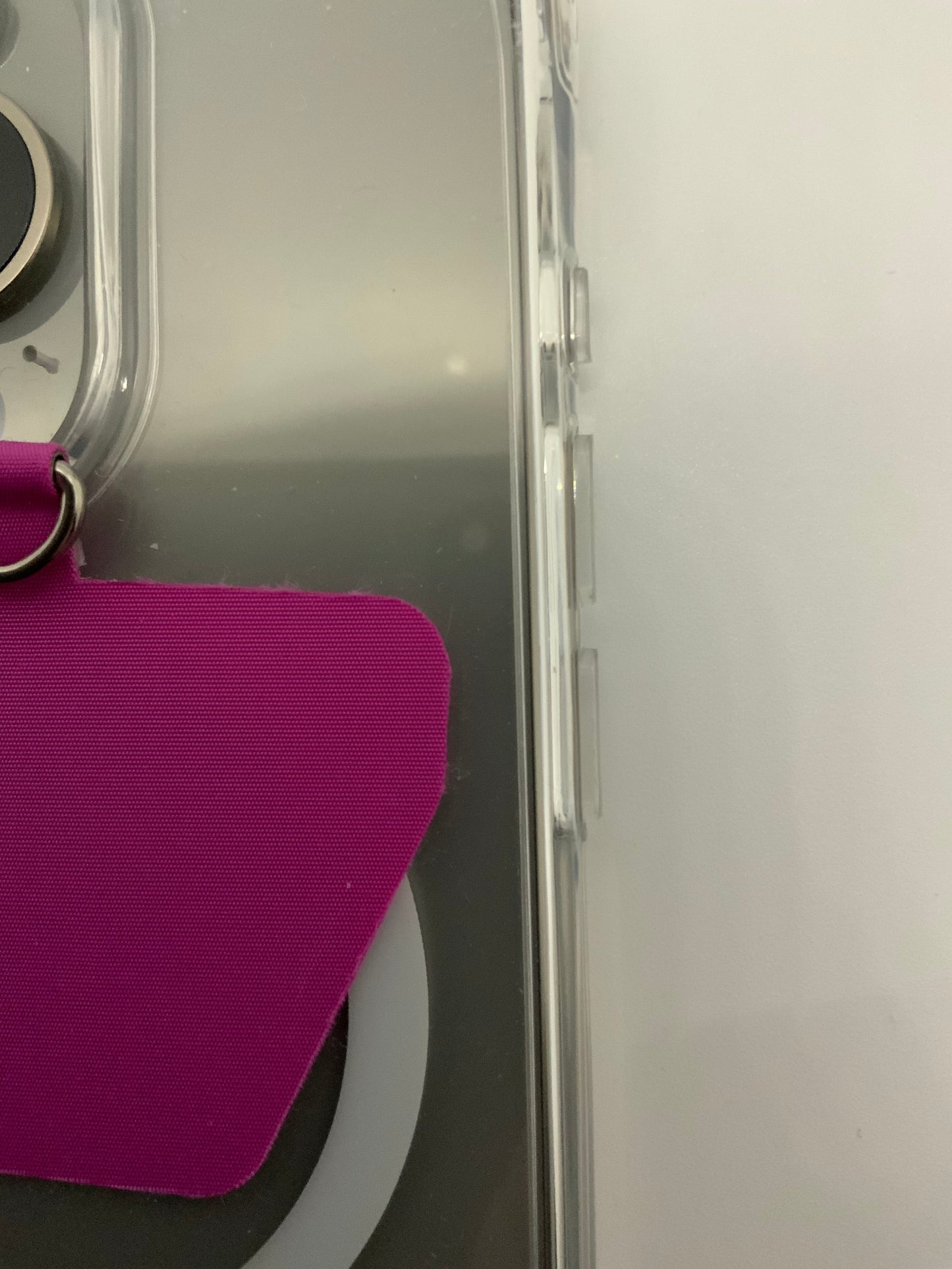 Be My AI: The picture shows a close-up of a few objects. On the left side, there is a clear plastic case with a silver ring attached to it. The ring has a purple strap connected to it. The plastic case seems to have a transparent cover and a clip on its side. On the right side of the image, there is a white surface. The bottom left corner shows a part of something that is black with a circular shape, but it's not fully visible in the picture.