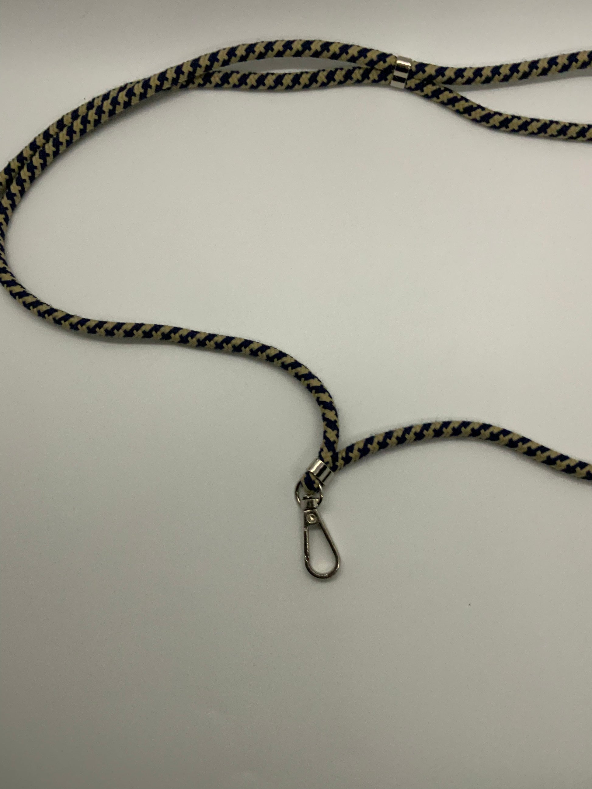 Be My AI: The picture shows a lanyard on a white background. The lanyard has a woven fabric strap with a zigzag pattern in black and yellow colors. At one end of the lanyard, there is a metal clasp that is silver in color. The clasp is shaped like a small carabiner, used to attach keys or an ID card. The lanyard also has a small metal piece that seems to be used for adjusting the length or position of the strap.