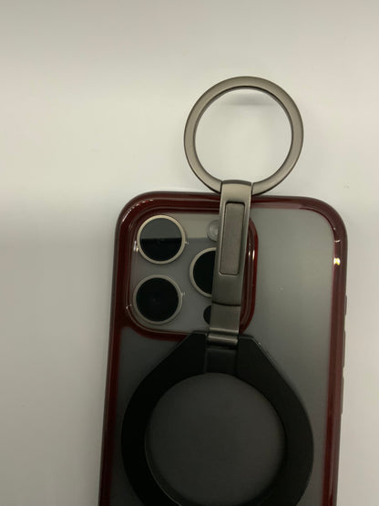 Be My AI: The picture shows a part of a smartphone with a case on it. The case is red and has a cut-out for the camera lenses. There are three camera lenses and a flash in the cut-out. Attached to the case is a silver ring holder that can be used to hold the phone securely or as a stand. The ring is attached to a base which is clipped onto the phone case. The background is plain white.