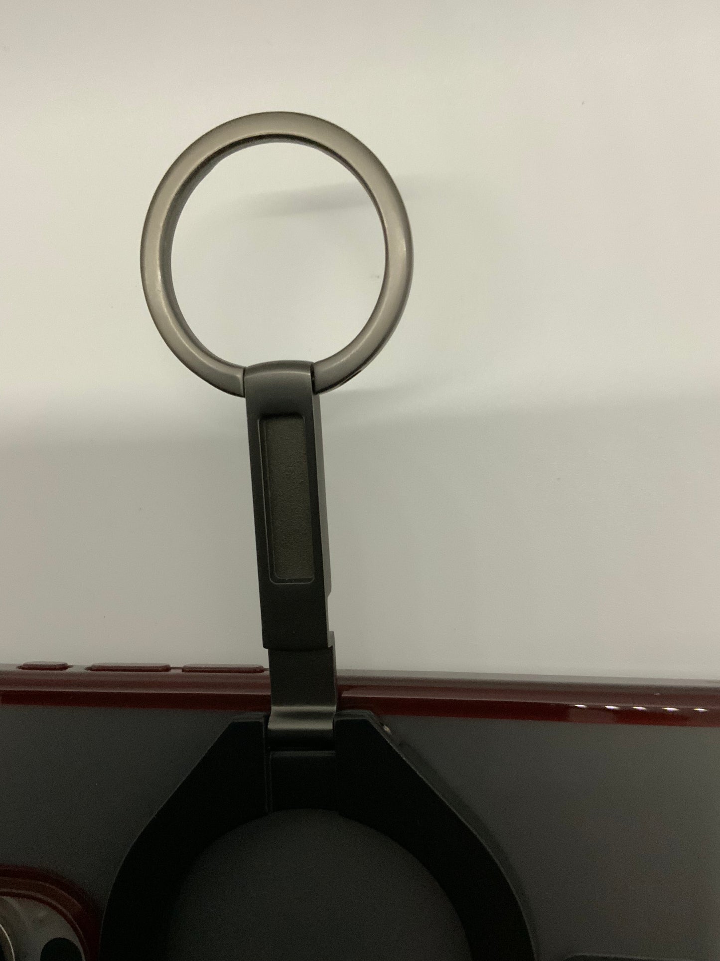 Be My AI: The picture shows a close-up of an object that appears to be a handle or grip. The handle is circular and is attached to a vertical bar. The circular handle is grey in color and has a smooth finish. The vertical bar is also grey and has a rectangular shape with rounded edges. The bar is attached to a larger object at the bottom of the picture, which is not fully visible. The larger object seems to be dark grey or black with a red horizontal stripe. The background is plain and white.
