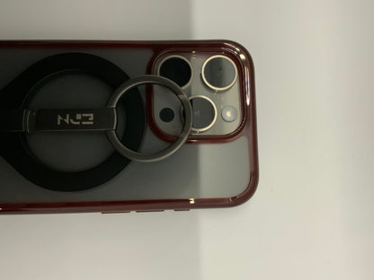 Be My AI: The picture shows a close-up of a few objects on a white surface. On the right side, there is a part of a phone with a red case. The phone has a camera module with three lenses and a flash. On the left side, there is a black object with a circular base and a metal ring attached to it. The metal ring is attached to a black rectangular piece with the letters "N" and "E" visible on it, suggesting that it might be a brand or model name. The objects are placed close to each other.
