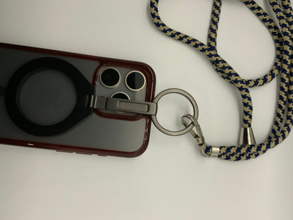 The picture shows a phone case with a lanyard attached to it. The phone case is burgundy in color and has a circular black attachment on the back, possibly for grip or as a stand. The case also has a cutout for the camera and flash, which are visible. The lanyard is made of a fabric material with a zigzag pattern in blue and beige colors. It is attached to the phone case through a metal ring and clip. The lanyard also has a small metal bell attached to it.