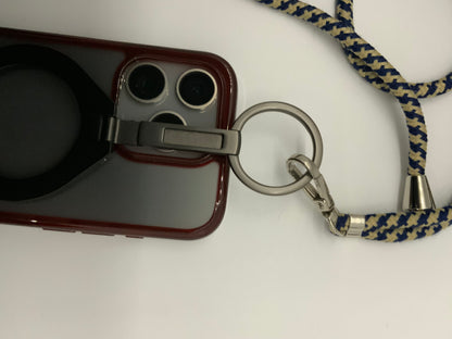 Be My AI: The picture shows a phone case with a strap attached to it. The phone case is red with a black circular attachment on the back, possibly for grip or as a stand. The case has a cutout for the camera and flash, which are visible. The strap is made of fabric with a blue and beige zigzag pattern. It is attached to the phone case through a silver metal ring and clip. The strap also has a small silver bell attached to it. The background is white.