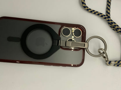 The picture shows an iPhone with a red case. On the back of the iPhone, there is a black circular attachment with an Apple logo in the center. The iPhone case has a cut-out for the camera, which shows three lenses and a flash.Attached to the iPhone case is a keyring with a fabric lanyard. The lanyard is blue with a yellow crisscross pattern. The keyring is silver and has a clip attached to it for easy attachment.