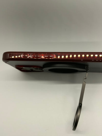 Be My AI: The picture shows a side view of a device that appears to be a tablet or a large smartphone. The device is in a horizontal position and has a deep red color. On the side of the device, there is a row of small LED lights that are illuminated. There are also what appears to be volume buttons and possibly a power button above the LED lights. The device is slightly elevated from the surface it is on, and there is a thin, silver-colored stand attached to the bottom of it, which is supporting it in the 
