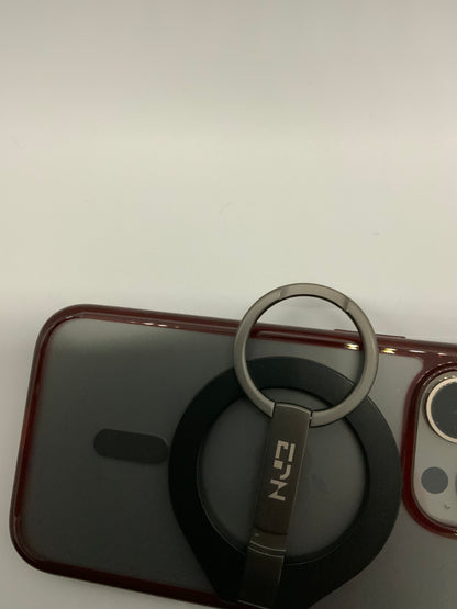 Be My AI: The picture shows a close-up of what appears to be the corner of a smartphone with a red case. Attached to the back of the phone is a circular black object with a metal ring. The metal ring is attached to a metal clip that has the letters "ETN" engraved on it. The background is plain and white. The smartphone's camera is also partially visible in the top right corner of the picture.