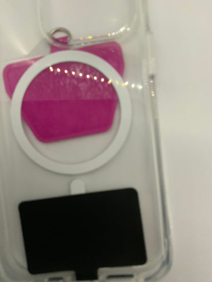 The picture is a bit blurry, but it appears to be of an object inside a clear plastic packaging. The object seems to be a pink, possibly glittery, item with a circular shape at the top and a rectangular shape at the bottom. There is a white ring around the pink item and a small metal ring attached to the top. The bottom part of the packaging has a black rectangular area. The background is white.