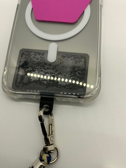 The picture shows a close-up of an object that seems to be a clear case with a few items attached to it. - There is a white rubbery loop with a small white tab attached to the case.- Above the loop, there is a pink rectangular object.- Below the loop, there is a black rectangular tag with a dotted white line across it.- Attached to the bottom of the case is a black clip with a silver metal hook.- There is also a blue and white braided string attached to the silver metal hook.The background