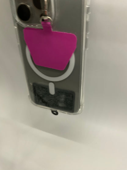 The picture shows a close-up of an object that appears to be a clear plastic case with a slot at the bottom. There is a small, rectangular, bright pink tag attached to the case through a metal ring. The tag is hanging from the top left corner of the case. The case has a circular cut-out on the front, and there is a small black and white label inside the case, visible through the cut-out. The background is white and slightly blurred.