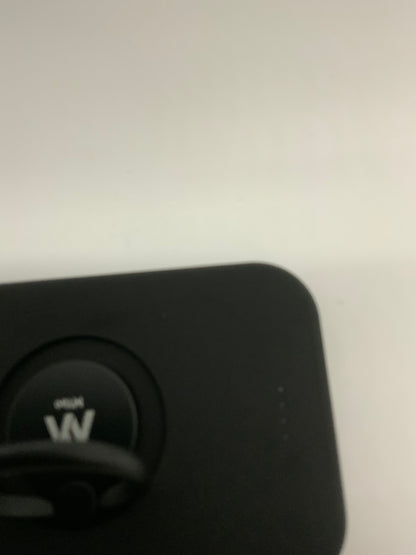 The picture shows a close-up of an object with a black surface. On the left side of the image, there is a circular button with a "W" on it. The button appears to be slightly recessed into the surface of the object. To the right of the button, there are four small dots in a vertical line, which might indicate some sort of status or level. The background of the image is a plain light color, possibly white or light grey.
