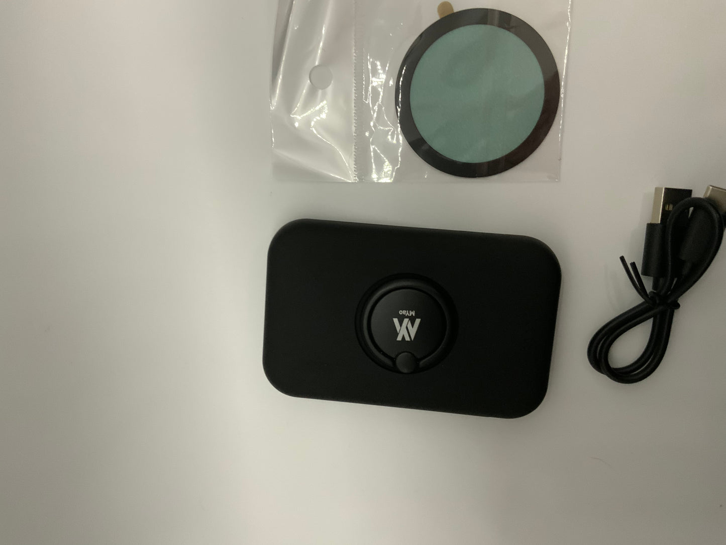The picture shows three items on a white surface:1. On the left, there is a small circular object in a clear plastic bag. The object appears to be a filter or a lens, with a greenish tint.2. In the center, there is a black rectangular device with rounded corners. It has a circular depression in the middle with the letters "XV" and the word "WARP" written below it in white.3. On the right, there is a black cable with USB connectors. The cable is coiled and appears to be new.The items are ne