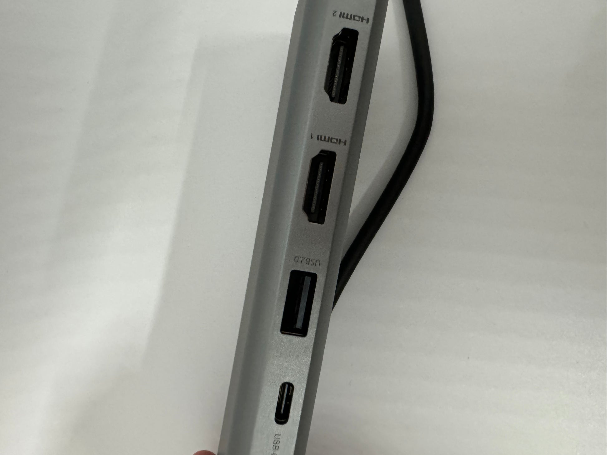 The picture shows a close-up of the side of a device, possibly a laptop or a hub, with multiple ports. The device is silver in color. There are three ports visible in the picture:1. The top port is labeled "HDMI" and appears to be an HDMI port.2. The middle port is also labeled "HDMI".3. The bottom port is labeled "USB" and appears to be a USB-C port.There is also a black cable running diagonally across the picture, but it's not connected to the device. The background is white.