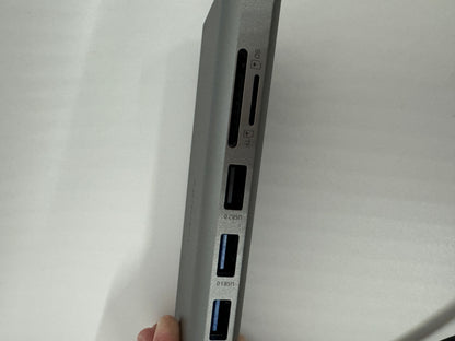 The picture shows the side of a grey electronic device, possibly a laptop or a hub, with multiple ports. From top to bottom, there is:- A slot labeled "SD" which is likely for SD memory cards.- A slot with a symbol that looks like a memory card, possibly for microSD cards.- Two USB ports labeled "USB3.0".There is also a part of a finger visible at the bottom, probably holding the device. The background is plain and white.