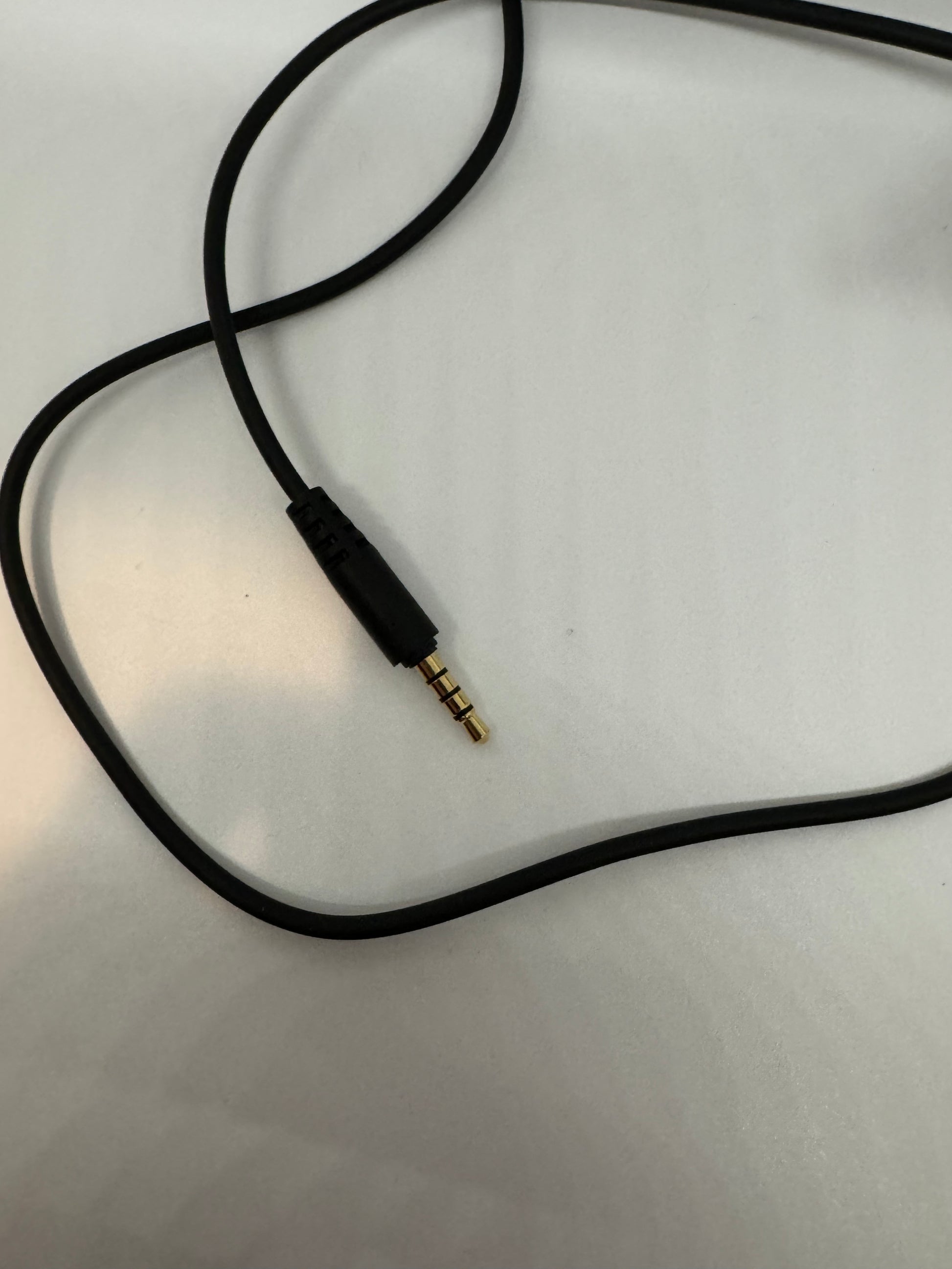 The picture shows a black audio cable on a white surface. The cable has a 3.5mm audio jack at one end. The jack has three bands on it, which usually indicates that it's a TRRS connector, often used for headphones that have a microphone built in. The cable appears to be in good condition.