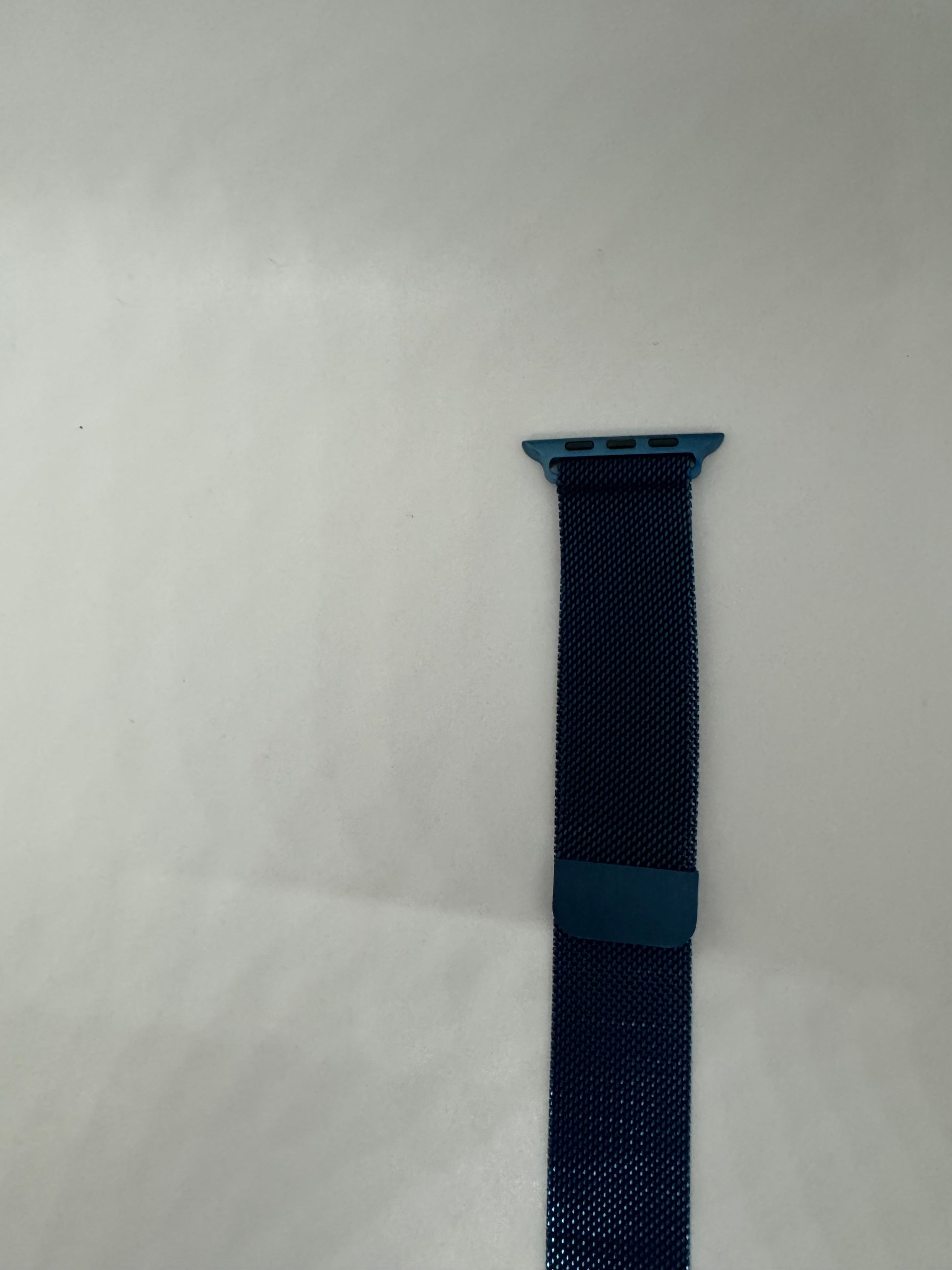 The picture shows a blue watch strap against a white background. The strap is made of a mesh material and has a loop to secure the excess strap. The top part of the strap has a connector with three holes, which is likely used to attach it to a watch. The strap is dark blue in color with a slightly lighter blue loop and connector.
