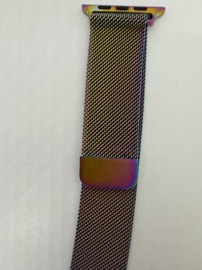 The picture shows a watch band. The band is made of a tightly woven metal mesh, giving it a flexible and smooth texture. The color of the band is a dark metallic, possibly a dark gray or black. The band has a small rectangular metal loop, which is likely used for adjusting the size. The loop has a reflective surface that shows a spectrum of colors, including purple and gold. The ends of the band have attachments that are likely used to connect it to a watch. The attachments are also reflective and