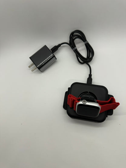 Be My AI: The picture shows a black portable wireless charger with a smartwatch on it. The smartwatch has a red band and is placed on the charging pad. The charger is connected to a black power adapter through a black cable. The power adapter has two prongs for plugging into an electrical outlet. The background is plain white.