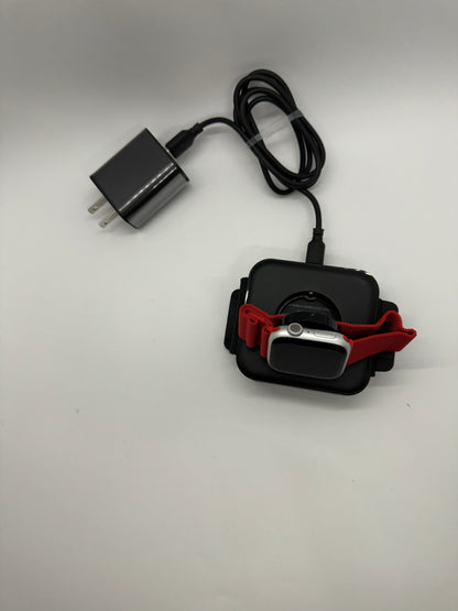 Be My AI: The picture shows two items on a white surface:

1. On the left side, there is a black charger with a two-prong plug and a black cable. The cable is coiled up and has a small black connector at the end.

2. On the right side, there is a smartwatch with a red band. The smartwatch is placed on a black wireless charging dock. The watch has a rectangular face with rounded corners and a single button on the right side. The red band is made of a woven material and is attached to the watch.

The charger 