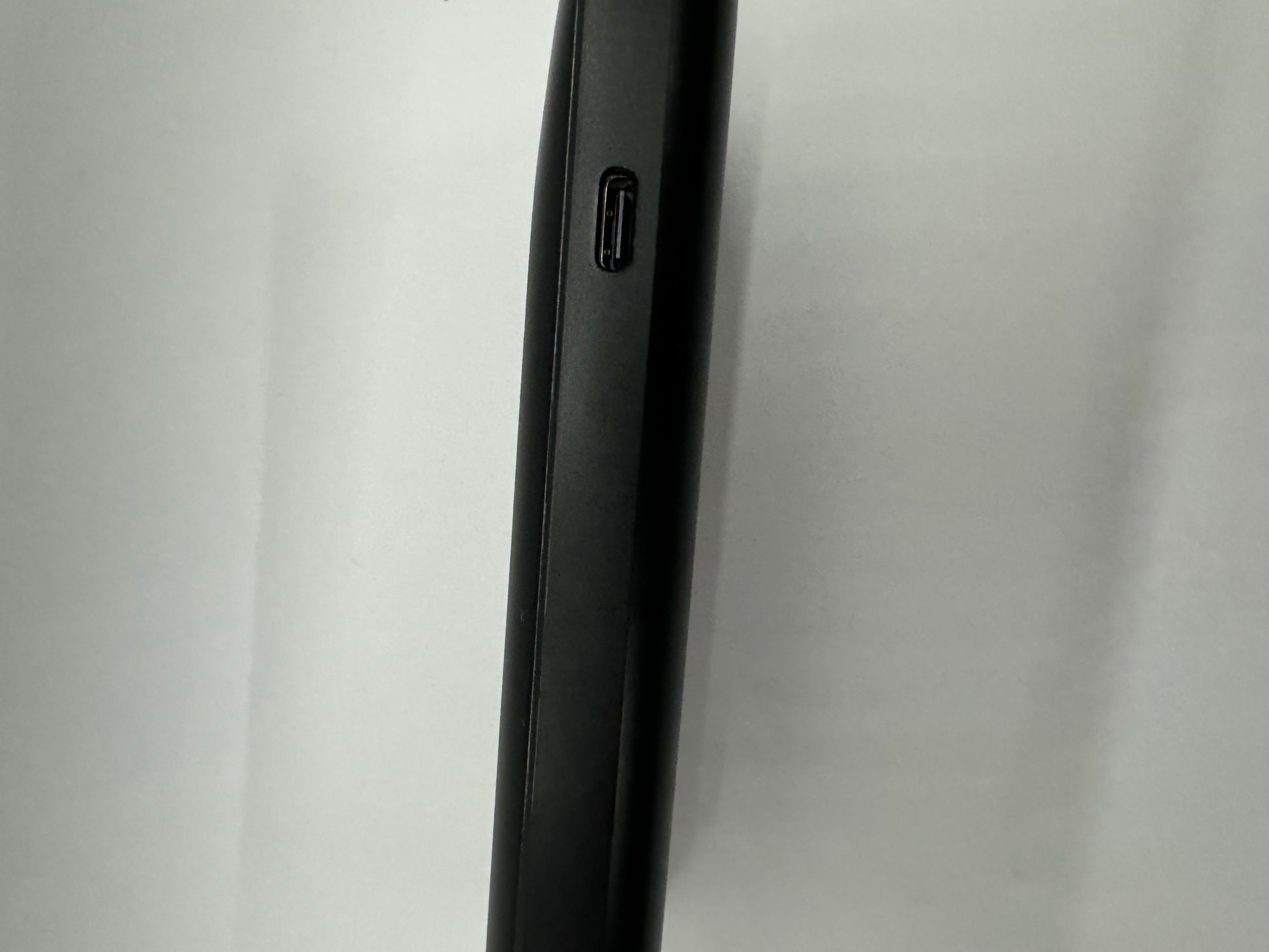 Be My AI: The picture shows a close-up of the side of a device, possibly a smartphone or tablet. The device has a black, slim edge. On this edge, there is a small port which looks like a USB port, likely used for charging or connecting to other devices. The background is plain and appears to be a light color, possibly white or light gray.