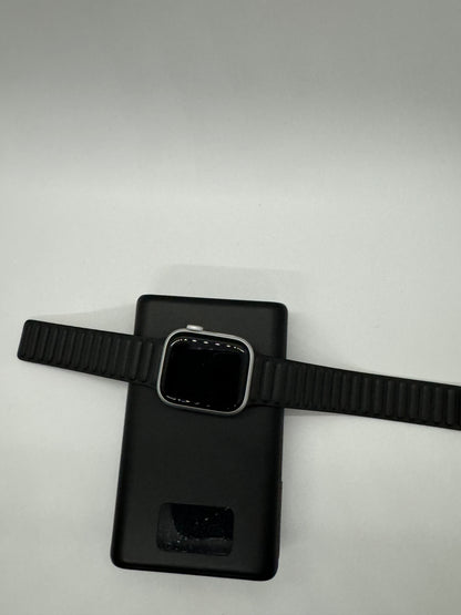 The picture shows a black smartwatch with a black strap, placed on top of a black smartphone. The smartwatch is positioned horizontally across the smartphone. The smartphone has a camera cutout near the top. The background is plain white.