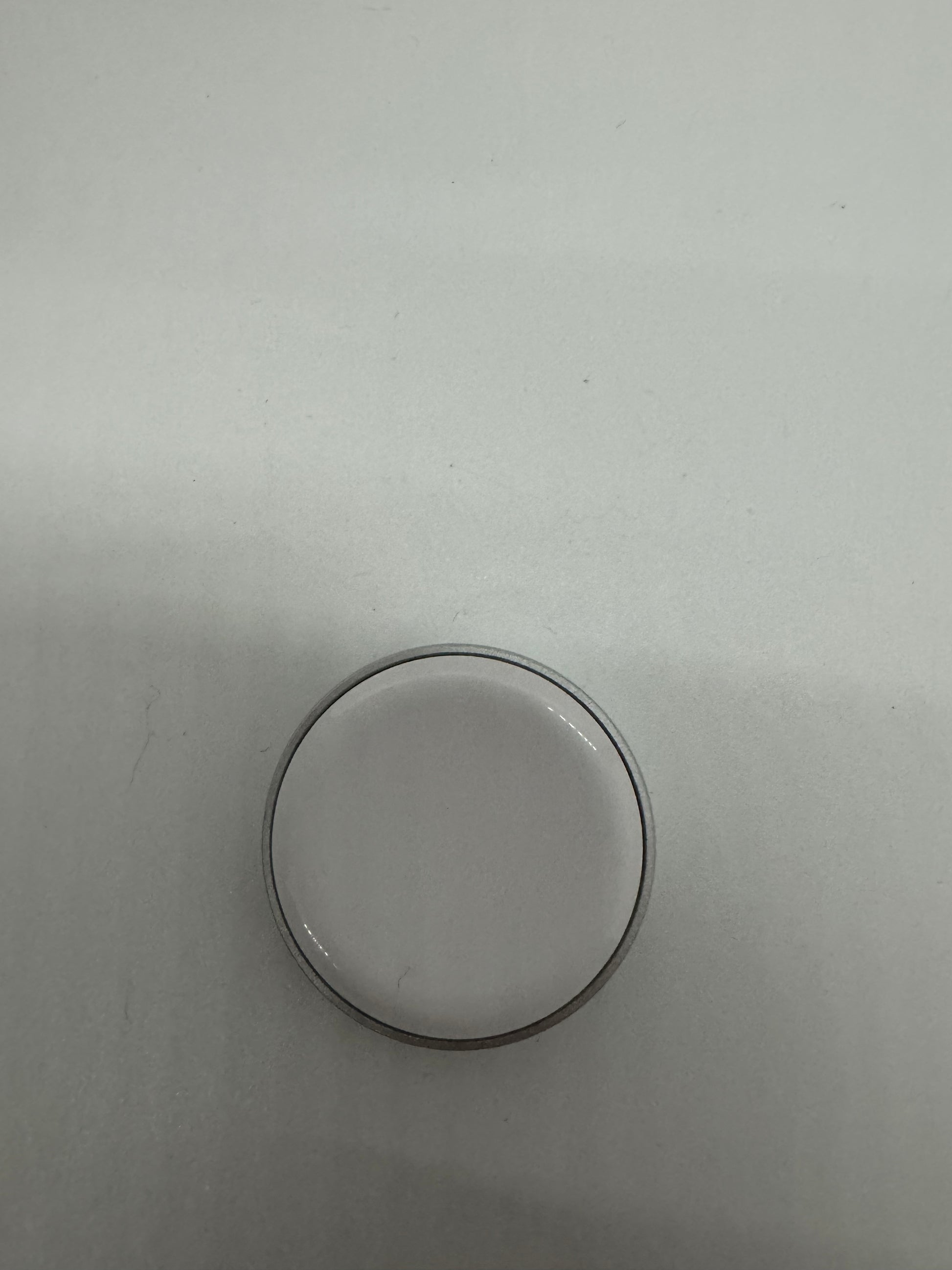The picture shows a small, circular object on a plain background. The object appears to be a ring or a band, possibly made of metal. It is thin and has a simple design. The background is a light color, and the object is placed towards the bottom of the image.