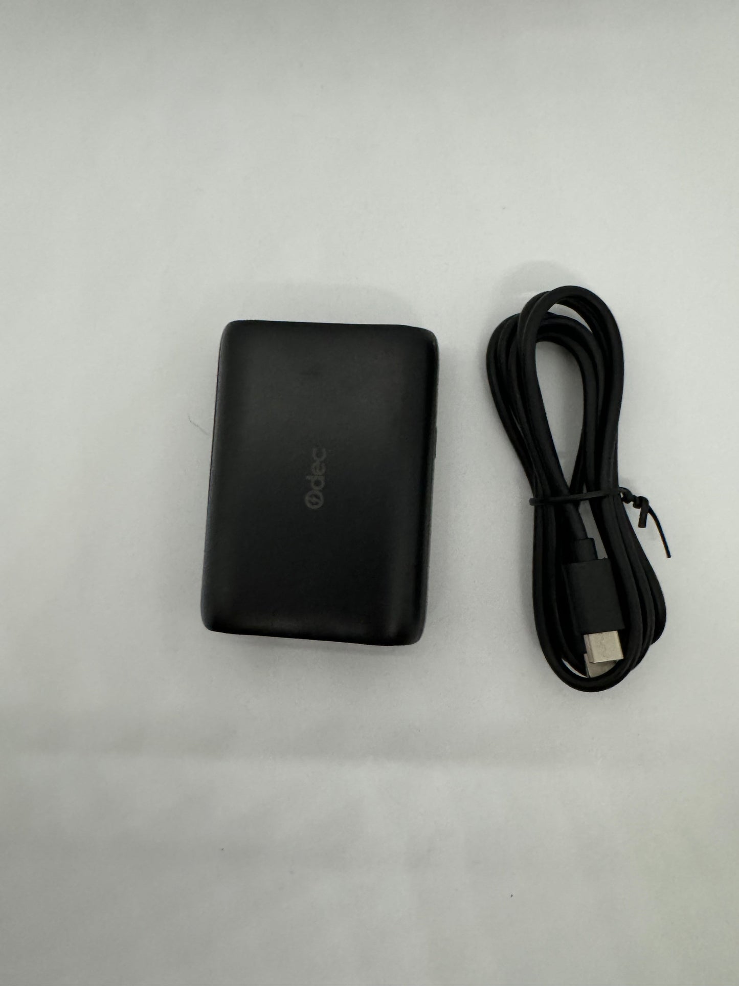 Be My AI: The picture shows two items on a white background. On the left, there is a black rectangular object that appears to be a portable charger or power bank. It has a matte finish and the letters "abc" are visible on it. On the right side of the picture, there is a black USB cable coiled up. The cable seems to be new or rarely used.
